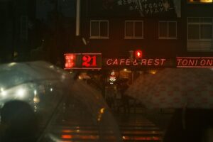Rainy city street with neon cafe signs at night.