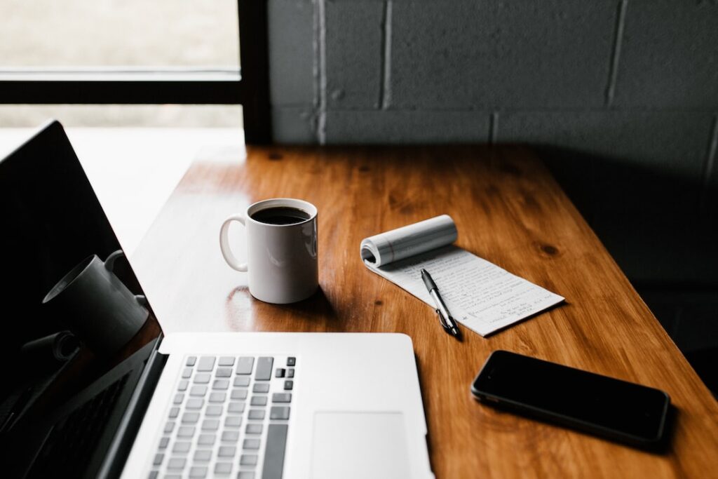 Workspace with laptop, coffee, notepad, and smartphone.