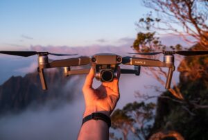 Hand holding a drone at sunset with mountain view.