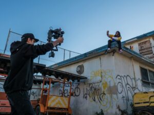 Filmmaker recording person on urban rooftop.