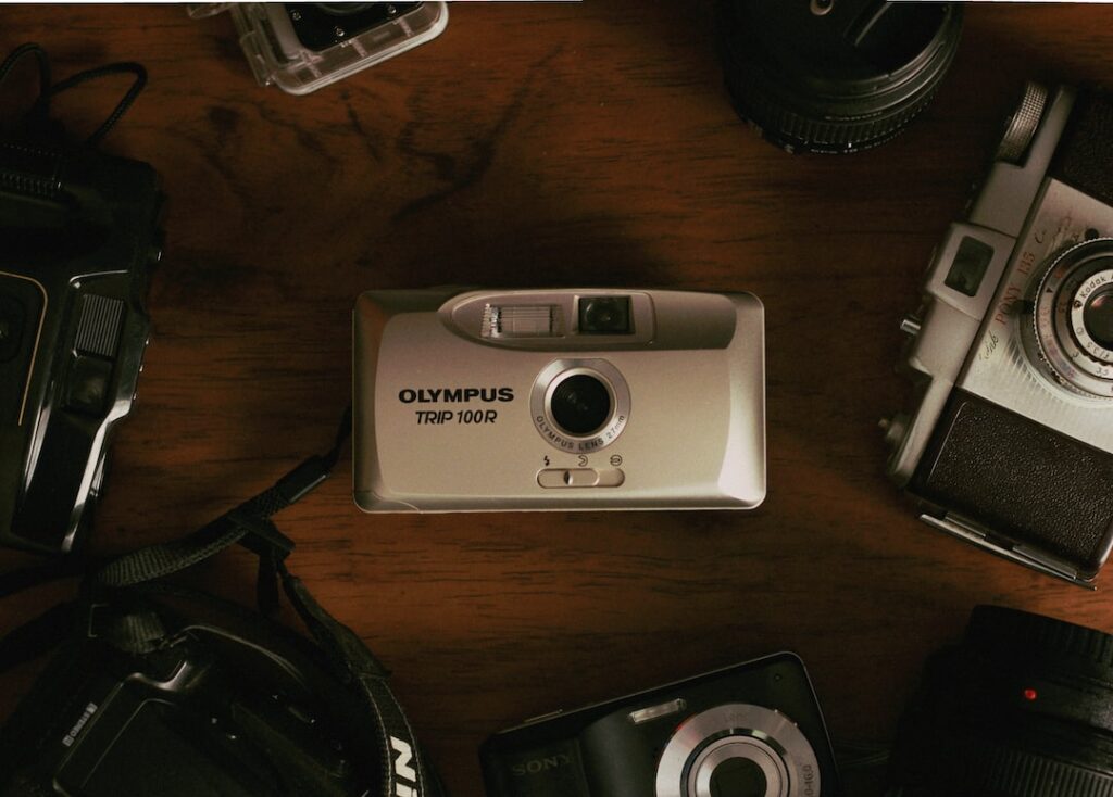 Vintage Olympus camera surrounded by various cameras on table.