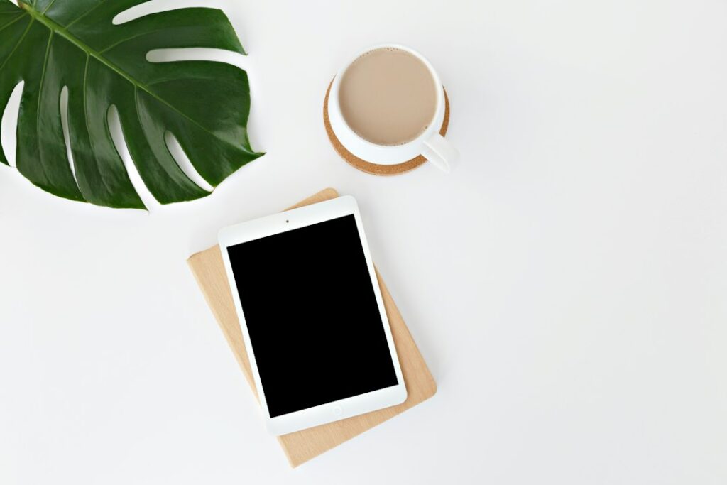 Minimalist desk with tablet, coffee, and monstera leaf.
