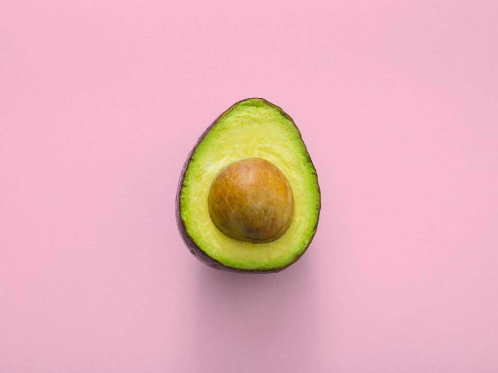 Halved avocado on pink background.
