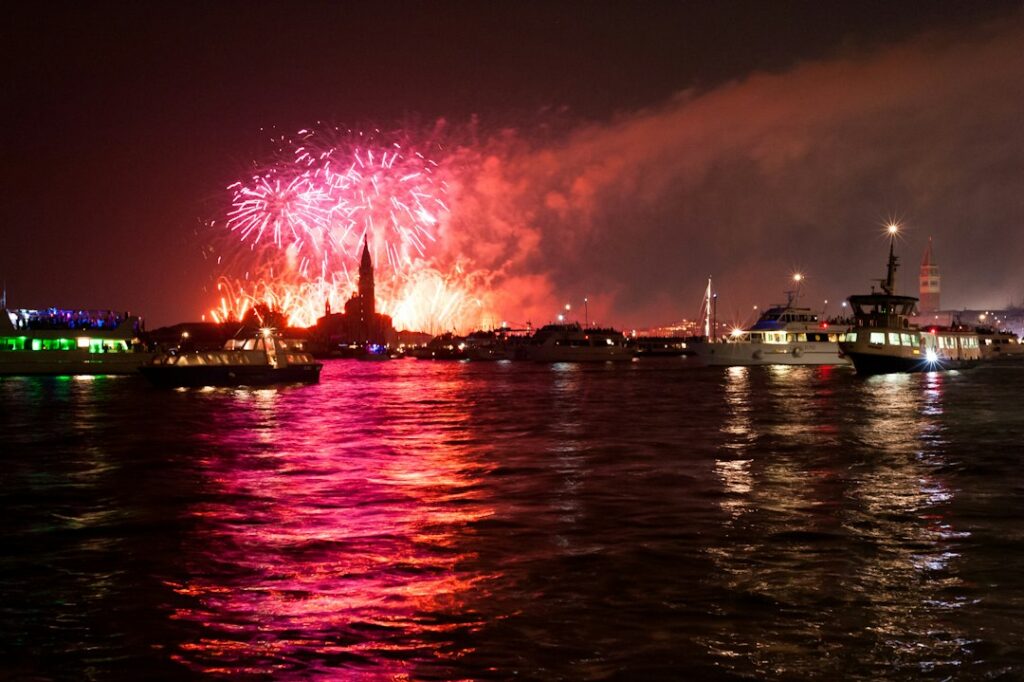 Fireworks display over water at night with boats.