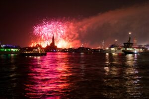 Fireworks display over water at night with boats.