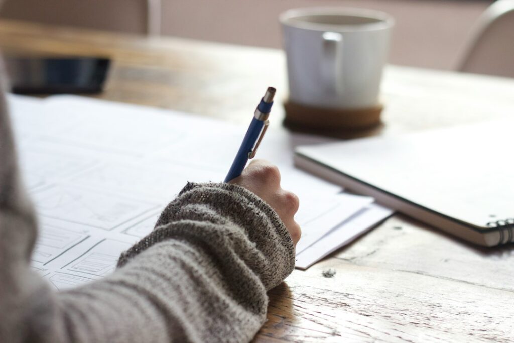 Person writing on paper beside coffee mug.