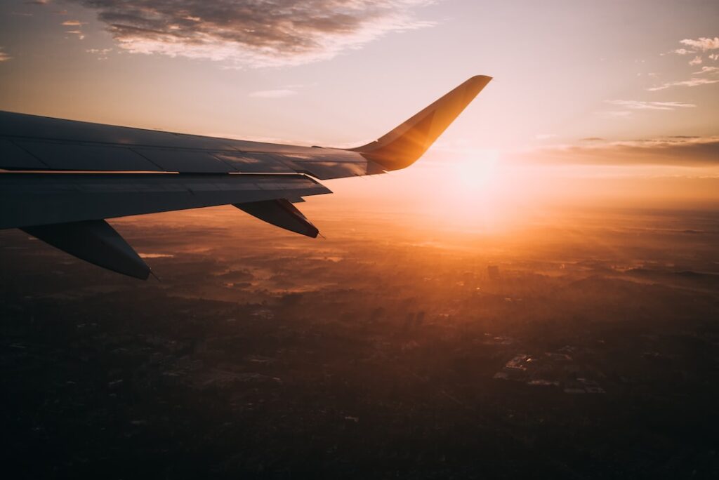 Airplane wing over city at sunset.