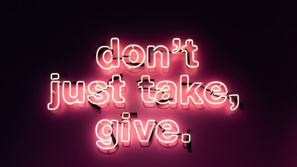 Neon sign "don't just take, give" on pink background.