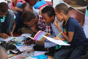 Children reading books together outdoors.