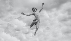 Man jumping against cloudy sky in monochrome
