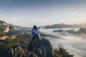 Photographer capturing misty mountain landscape at sunrise