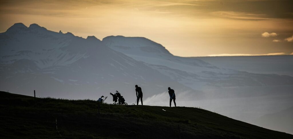 Silhouetted golfers playing against mountain sunset backdrop