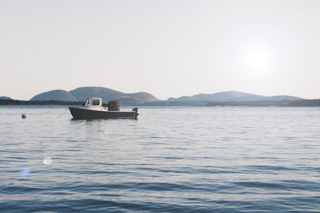 Boat on calm water with distant hills at sunrise.