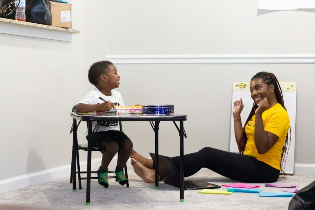 Child coloring with smiling woman sitting on floor.