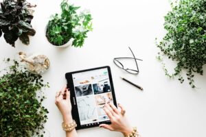 Person browsing tablet amid plants and office supplies.