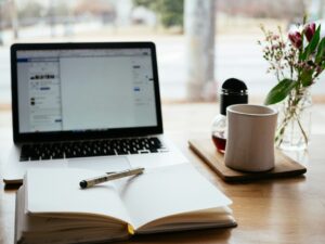 Laptop, notebook, and coffee on a desk.