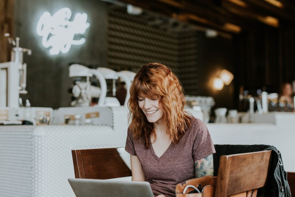 Woman smiling while using laptop in cafe.