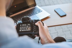 Person reviewing camera settings beside laptop and smartphone.