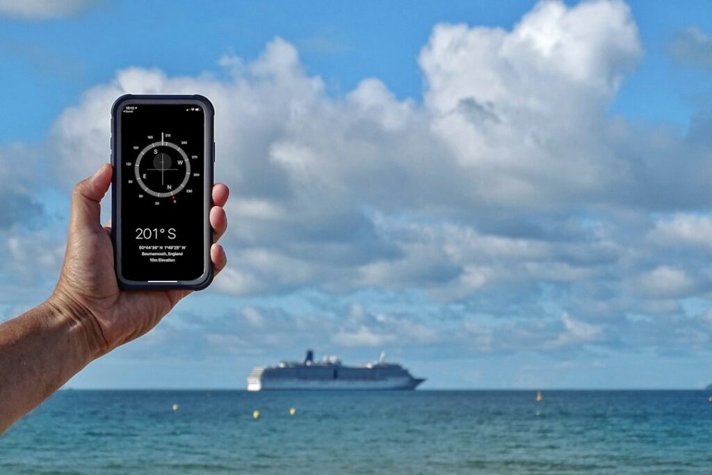 Hand holding smartphone compass app with cruise ship background.