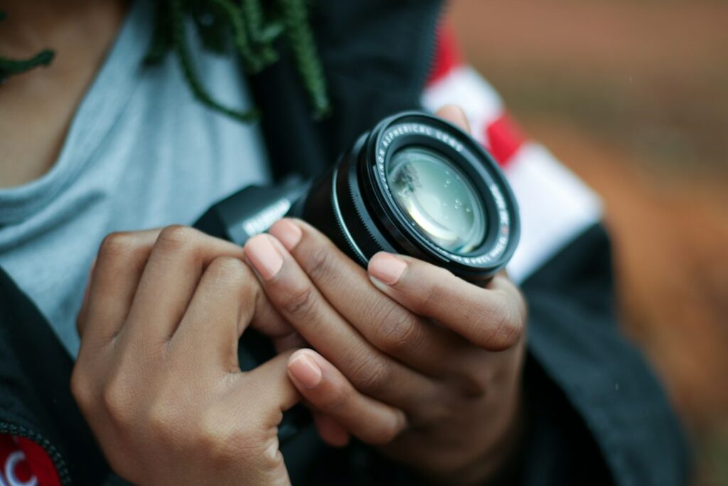 Person holding camera lens outdoors.