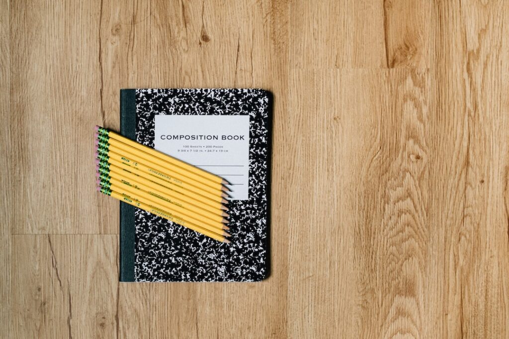 Composition notebook and pencils on wooden surface.