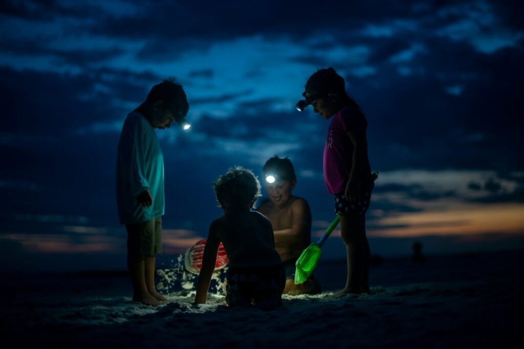 Children playing on beach at dusk with flashlights.